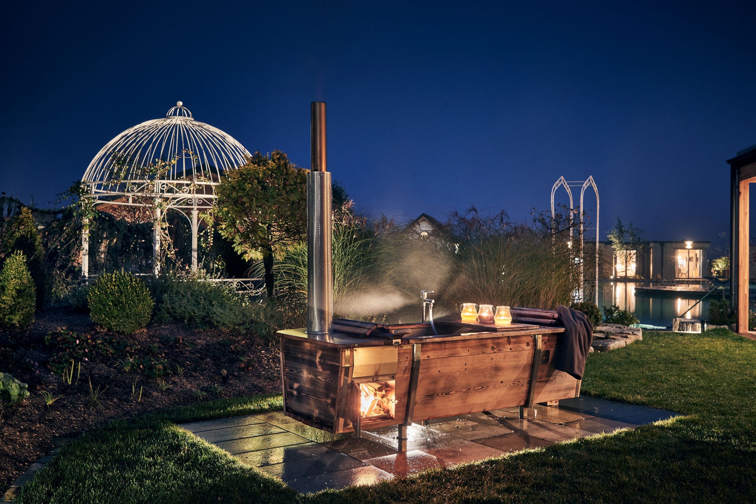 Gartenbadewanne aus Hol mit geflämmtem Holz und Holzofen bei Nacht