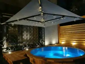 Feuerwasser Hot Tub aus V4A-Edelstahl und Kiefernholz bei Nacht mit blauem Wasser und Lichterkette