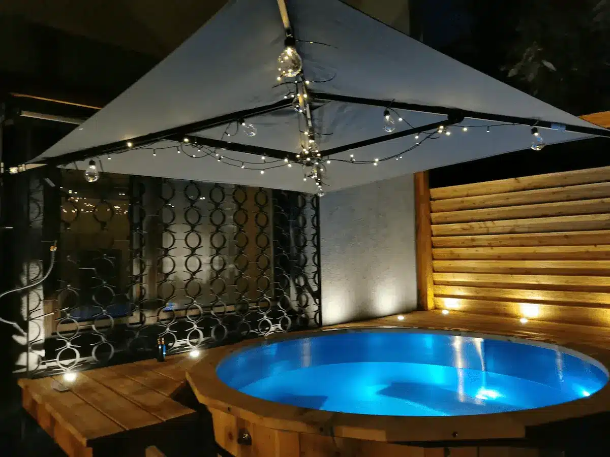 Feuerwasser Hot Tub aus V4A-Edelstahl und Kiefernholz bei Nacht mit blauem Wasser und Lichterkette