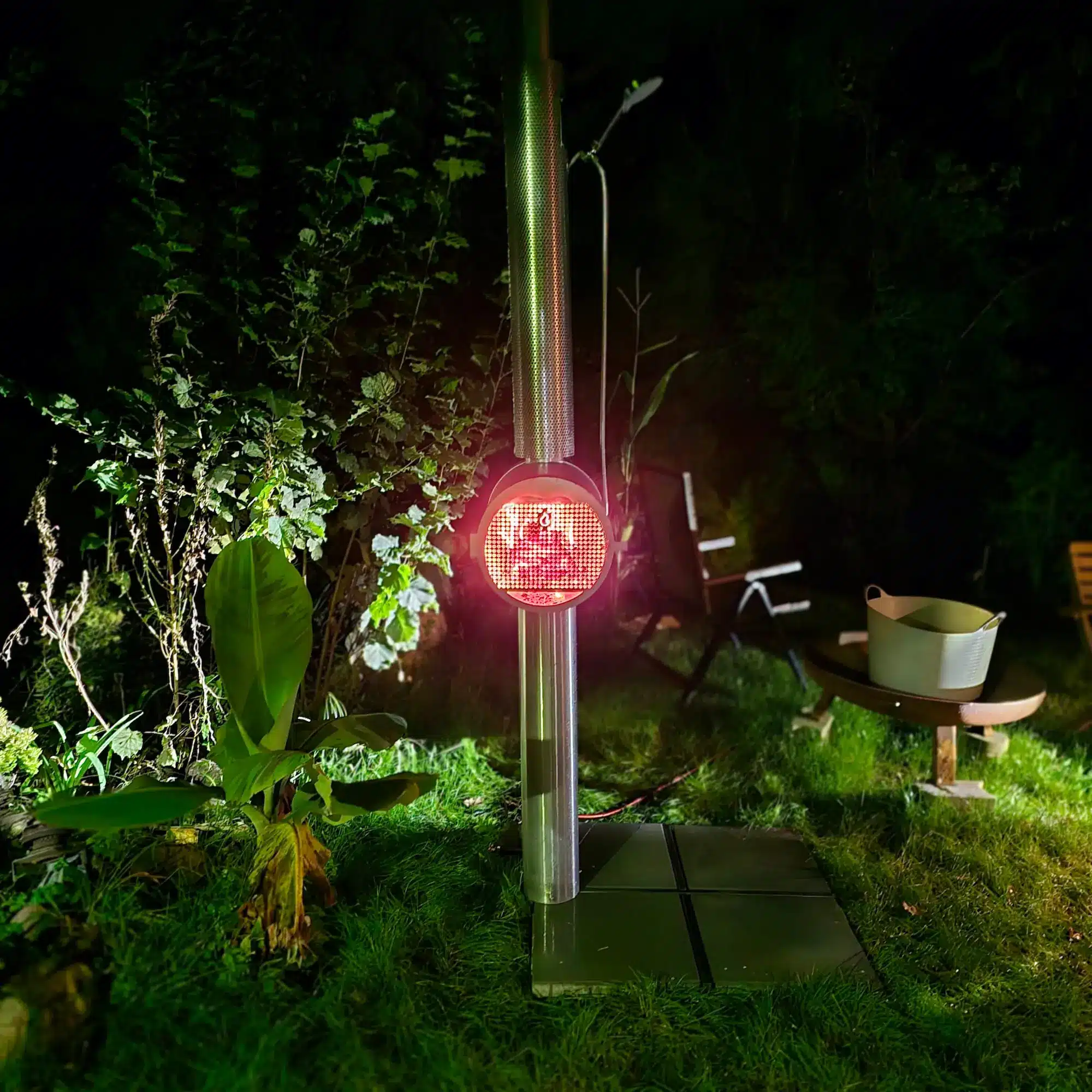 Feuerwasser Edelstahl-Gartendusche bei Nacht mit brennendem Feuer im Garten