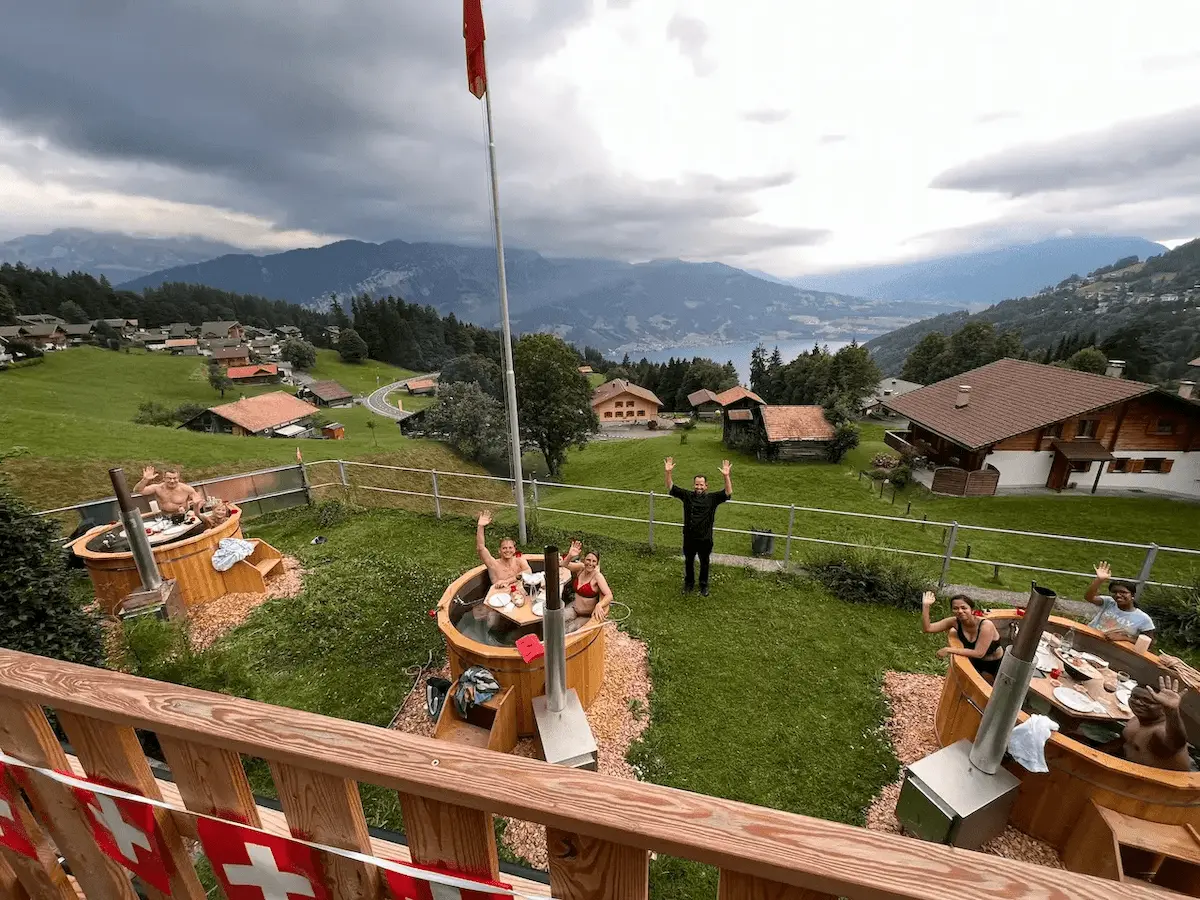 Gäste genießen ein Fondue in drei beheizten Feuerwasser-Badefässern mit Blick auf Thunersee, Eiger, Mönch und Jungfrau im Hotel Beatenberg Fassbind.