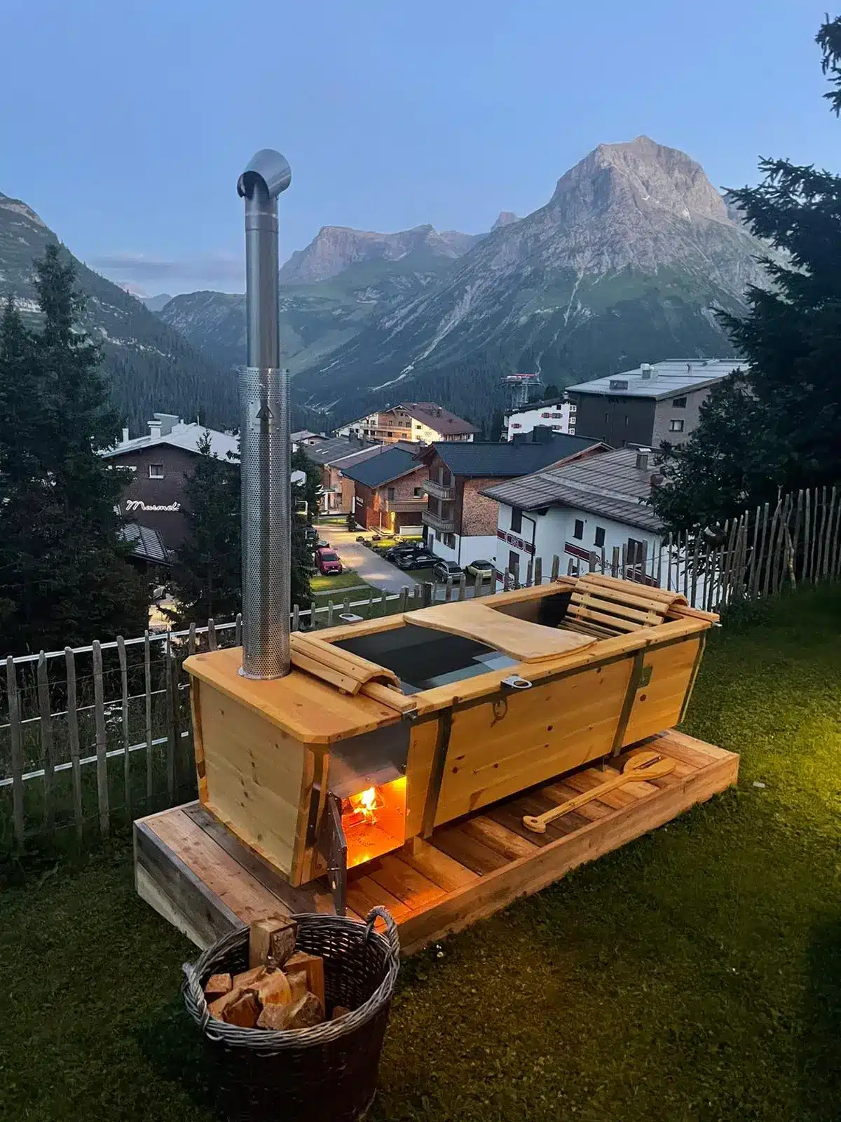 Feuerwasser Outdoor-Badewanne aus V4A-Edelstahl und Kiefernholz mit Blick auf Lech am Arlberg in der Abenddämmerung