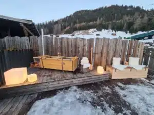 Outdoor-Badewanne von Feuerwasser auf winterlicher Almhütte mit Holzofen und Bergkulisse