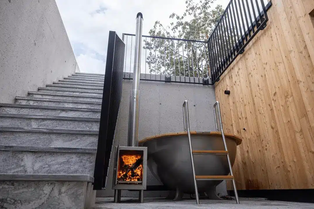 Beheizbarer Edelstahl-Badezuber von Feuerwasser im Penthouse Chalet – modern eingebaut zwischen Betonwand, Holzfassade und Außentreppe