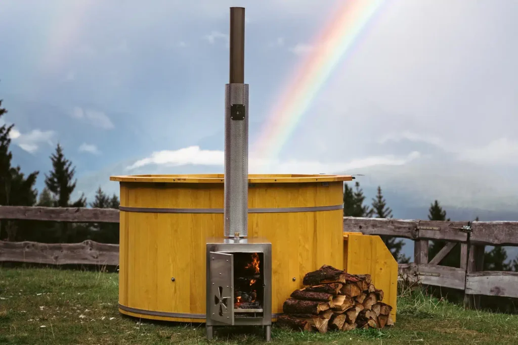 Solid pine wood hot tub with V4A stainless steel stove in front of a mountain panorama and rainbow of firewater